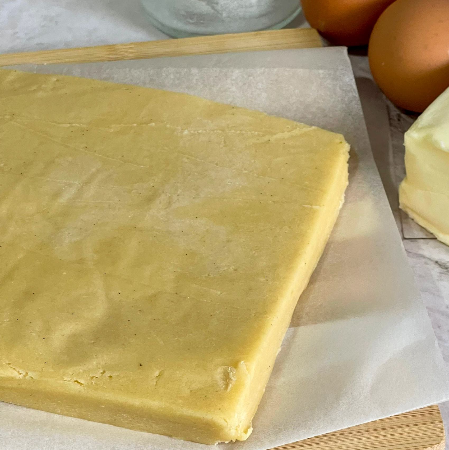 Un pezzo di pasta è appoggiato su un pezzo di carta oleata accanto a uova e burro