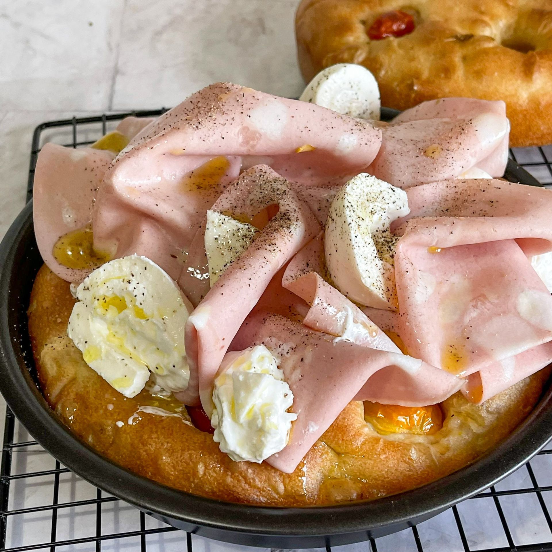 Una pizza con prosciutto e formaggio è appoggiata su una griglia di raffreddamento.