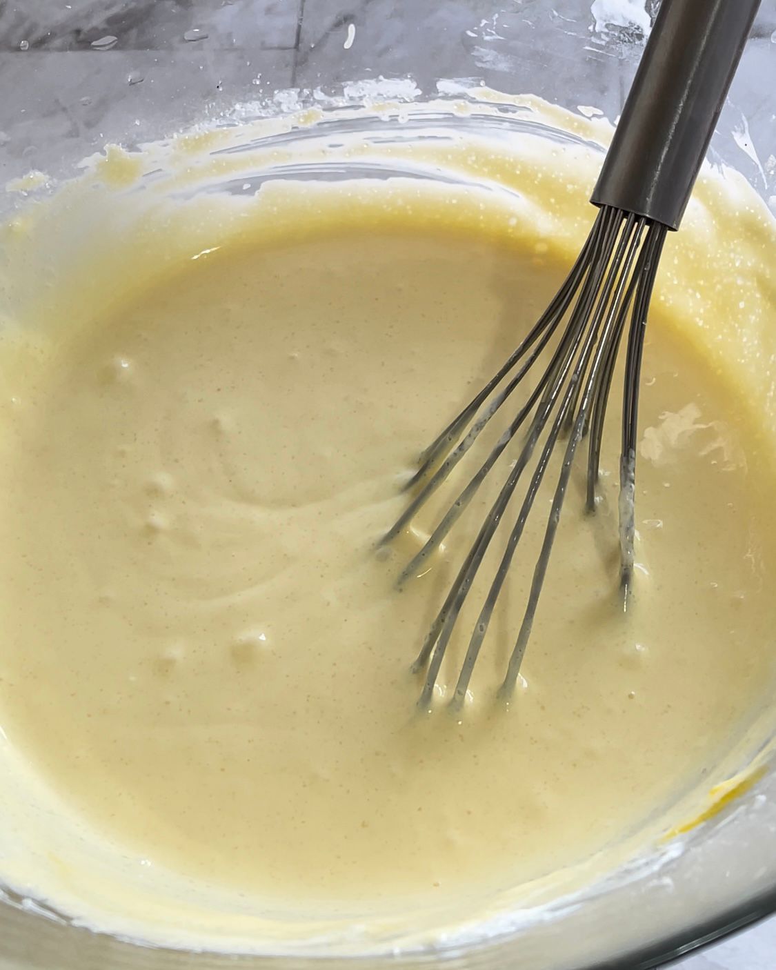 Una frusta mescola un liquido giallo in una ciotola di vetro