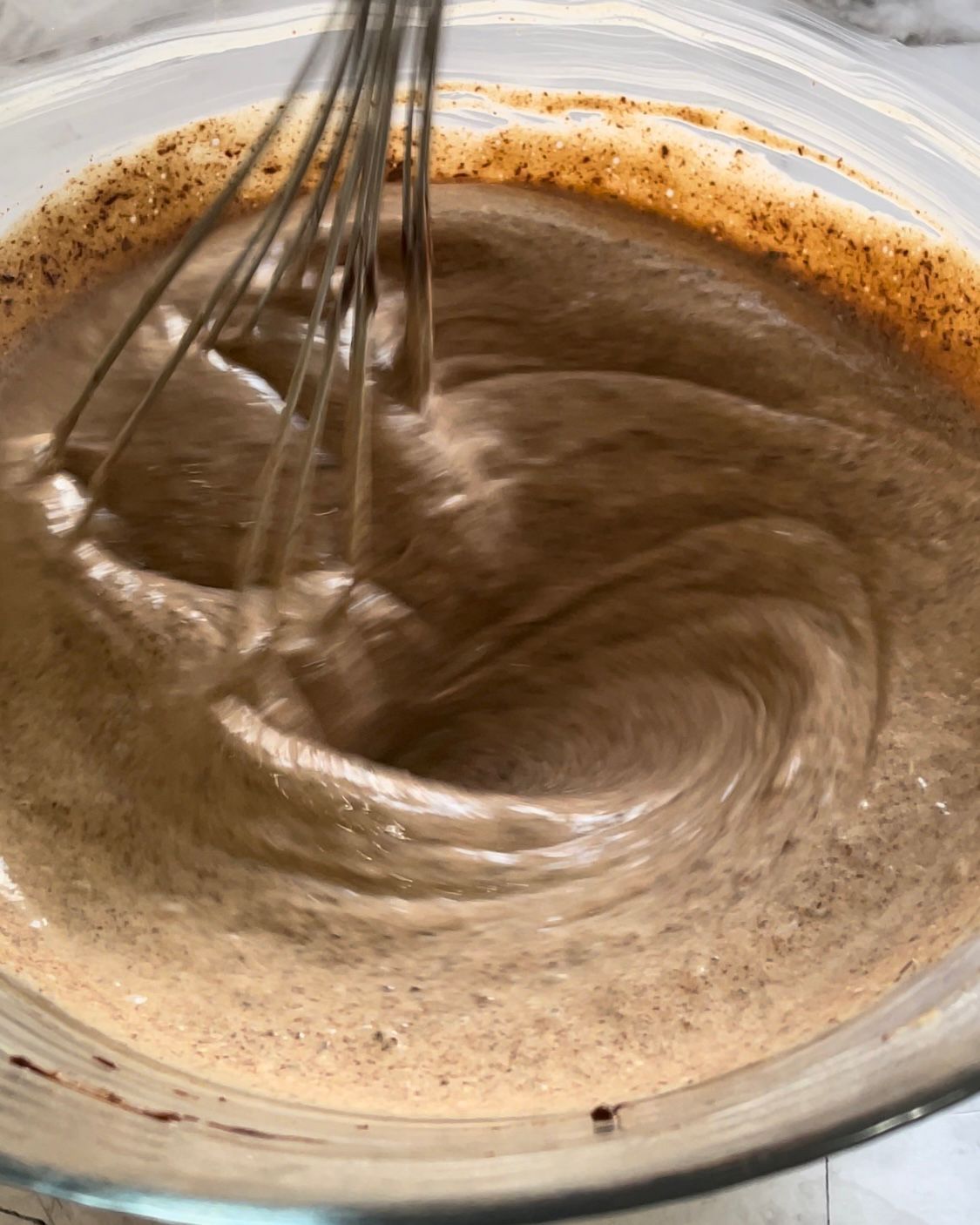 Si usa una frusta per mescolare un liquido marrone in una ciotola di vetro.