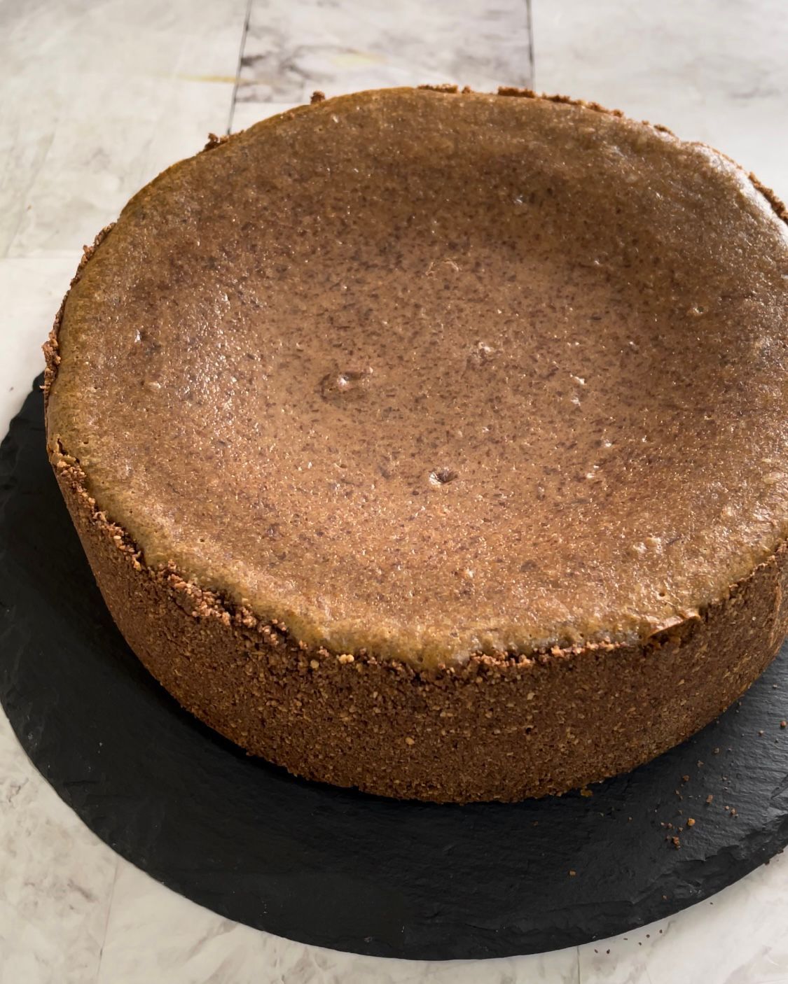 Una torta marrone è appoggiata su un piatto nero su un tavolo.
