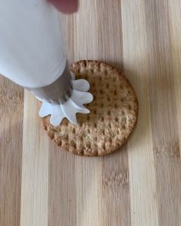 Una persona sta versando la glassa su un cracker su un tavolo di legno.