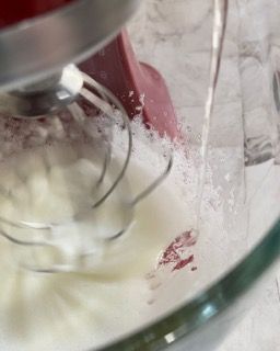 Primo piano di un mixer che prepara la panna montata in una ciotola di vetro.