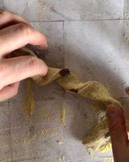Una persona tiene in mano un pezzo di pasta su un tavolo.