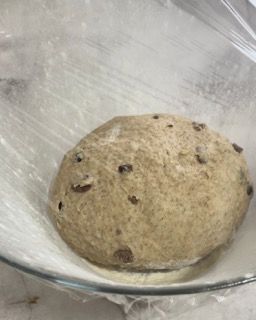 Una palla di pasta è posta in una ciotola di vetro ricoperta di pellicola trasparente.