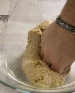 Una persona sta impastando l'impasto in una ciotola di vetro.
