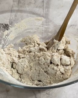 Una ciotola di vetro piena di farina e un cucchiaio di legno.