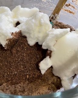Un primo piano di una ciotola di torta al cioccolato con panna montata e una spatola.