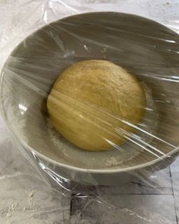 Una palla di pasta in una ciotola coperta con pellicola trasparente.