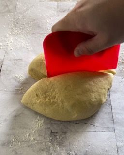 Una persona sta usando una spatola rossa per stendere l'impasto su un tavolo.