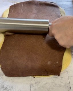 Una persona sta stendendo un pezzo di pasta al cioccolato con un mattarello.