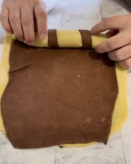 Una persona sta stendendo un pezzo di pasta marrone e gialla.
