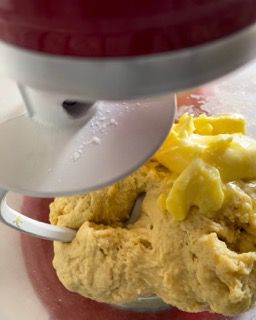 Un primo piano di un mixer con impasto e burro dentro