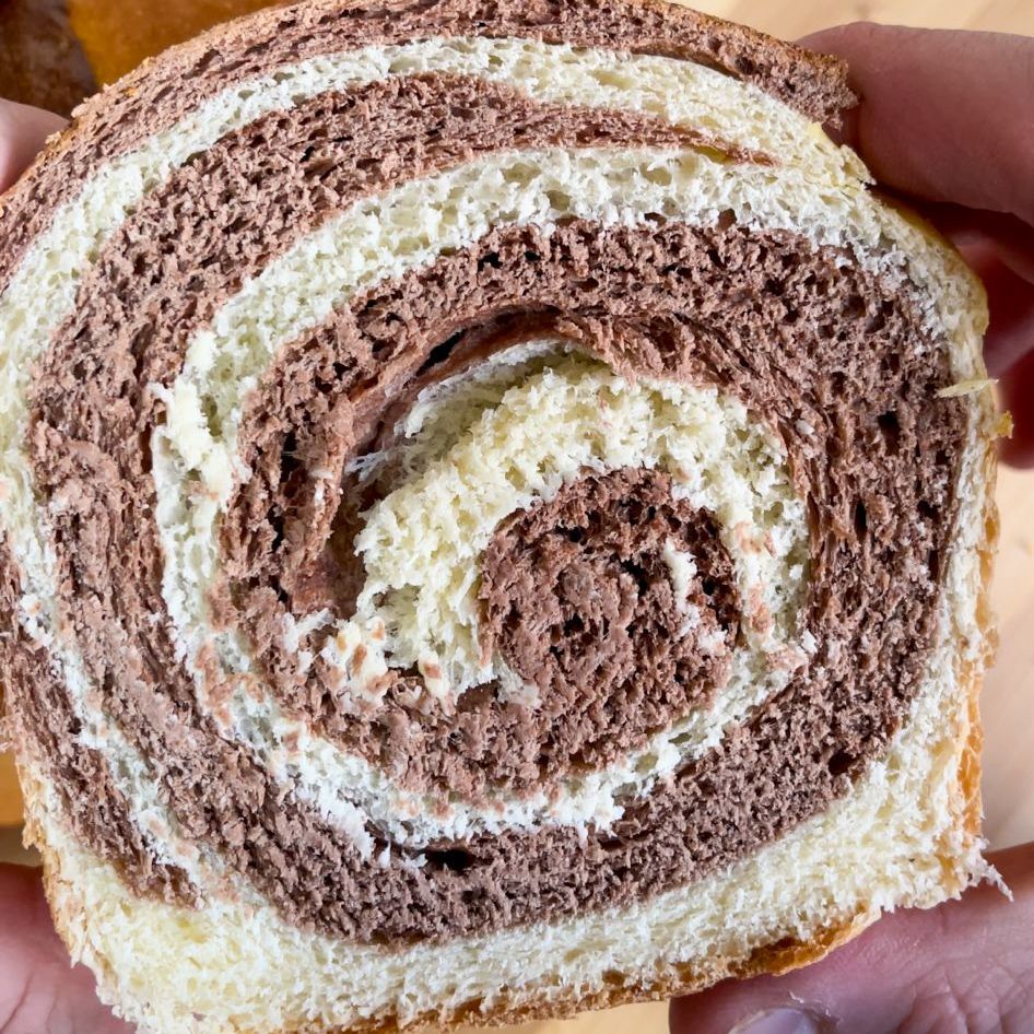 Una persona tiene in mano un pezzo di cioccolato e del pane bianco.