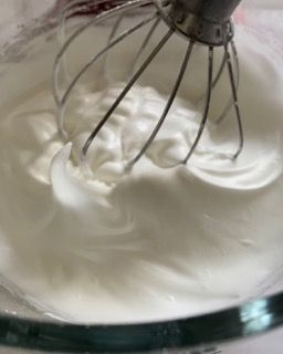 Primo piano di una frusta in una ciotola di panna montata.