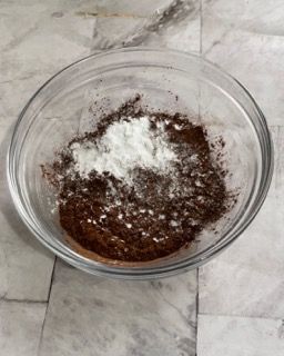 Una ciotola di vetro piena di cioccolato e farina su una superficie di marmo.