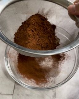 Una persona sta setacciando il cacao in polvere in una ciotola di vetro.
