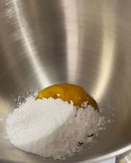 Una ciotola di acciaio inossidabile piena di zucchero a velo e un uovo.