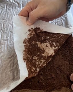 Una persona tiene in mano un pezzo di torta al cioccolato su un foglio di carta oleata.