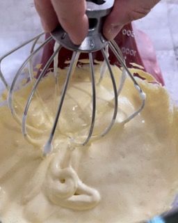 Una persona tiene una frusta sopra una ciotola di pastella