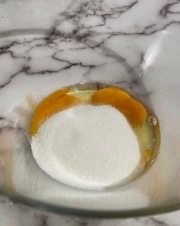 Un primo piano di una ciotola di zucchero e uova su un tavolo.