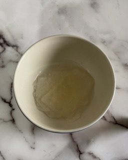 Una ciotola bianca piena di liquido è appoggiata su una superficie di marmo.