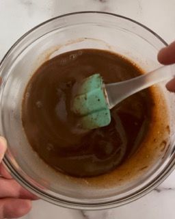 Una persona tiene in mano una ciotola piena di liquido marrone con un cucchiaio dentro.