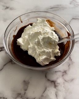 Una ciotola di budino al cioccolato con panna montata e un cucchiaio dentro.