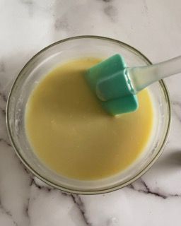 Una ciotola di liquido giallo con una spatola verde dentro.