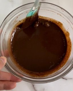 Una persona tiene in mano una ciotola di salsa al cioccolato con un cucchiaio dentro.