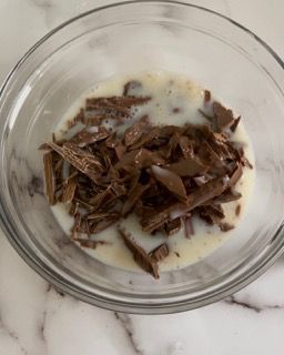 Una ciotola di vetro piena di scaglie di cioccolato e latte su un tavolo.