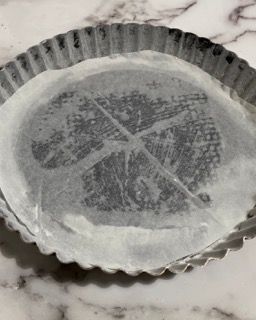 Una teglia per torta ricoperta di carta oleata è appoggiata su un tavolo.