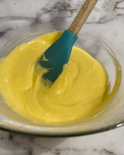 Una ciotola di salsa gialla con una spatola blu dentro.
