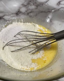 Una frusta è in una ciotola con farina e uovo.