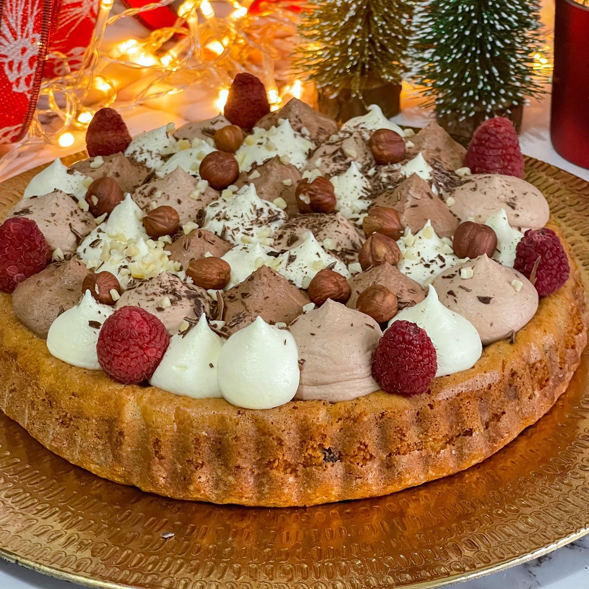 Una torta con lamponi, cioccolato, panna montata e nocciole su un piatto d'oro.