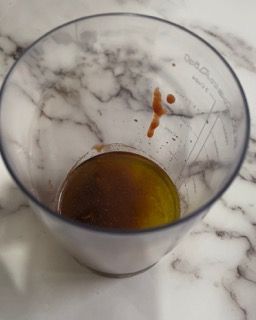 Una tazza graduata trasparente piena di liquido marrone su una superficie di marmo.