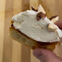Una persona tiene in mano un pezzo di torta con panna montata e mandorle sopra.