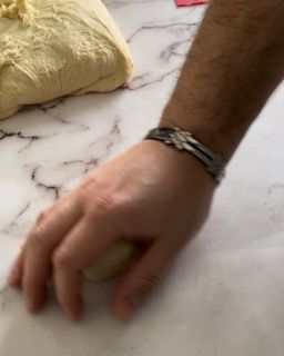 Un primo piano della mano di una persona che stende la pasta su un tavolo.