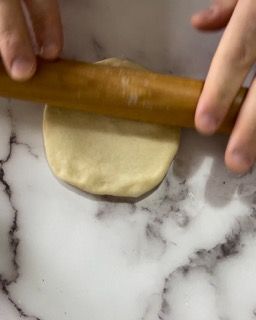 Una persona sta stendendo la pasta con un mattarello su una superficie di marmo.