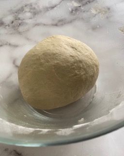 Una palla di pasta è appoggiata su una ciotola di vetro su un tavolo.