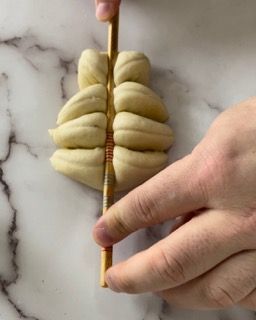 Una persona tiene un bastoncino di legno sopra un pezzo di impasto.