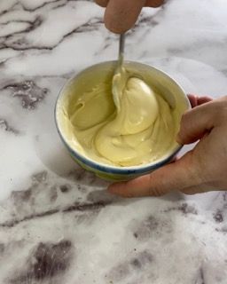 Una persona tiene in mano una ciotola di maionese con un cucchiaio dentro.