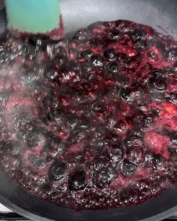 Una padella piena di salsa di frutti di bosco viene mescolata con una spatola.