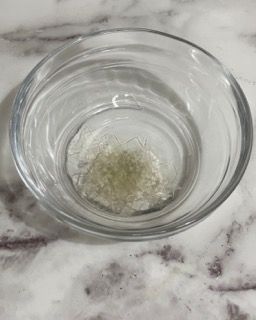 Una ciotola di vetro piena d'acqua e un piccolo pezzo di cibo su un tavolo.