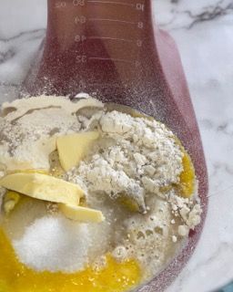 Una tazza graduata piena di farina, burro e uova.