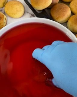 Una persona che indossa un guanto blu sta toccando una ciotola di liquido rosso