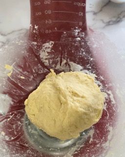 Una ciotola di impasto è appoggiata su un tavolo accanto a un misurino.