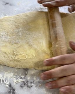 Una persona sta stendendo la pasta con un mattarello su un tavolo.