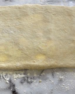 Un pezzo di pasta è appoggiato su un tavolo ricoperto di farina.