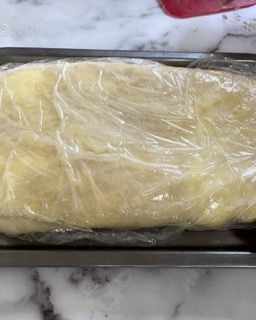 Una pagnotta di pasta avvolta nella pellicola trasparente su un vassoio su un tavolo.